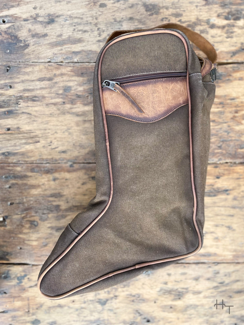 Photo of back of boot bag made with brown canvas and leather accents with zipper pocket and wood background