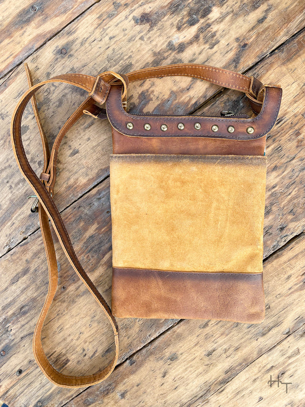 Photo of back side of brown leather crossbody purse with rivet accents and long crossbody strap with wood background