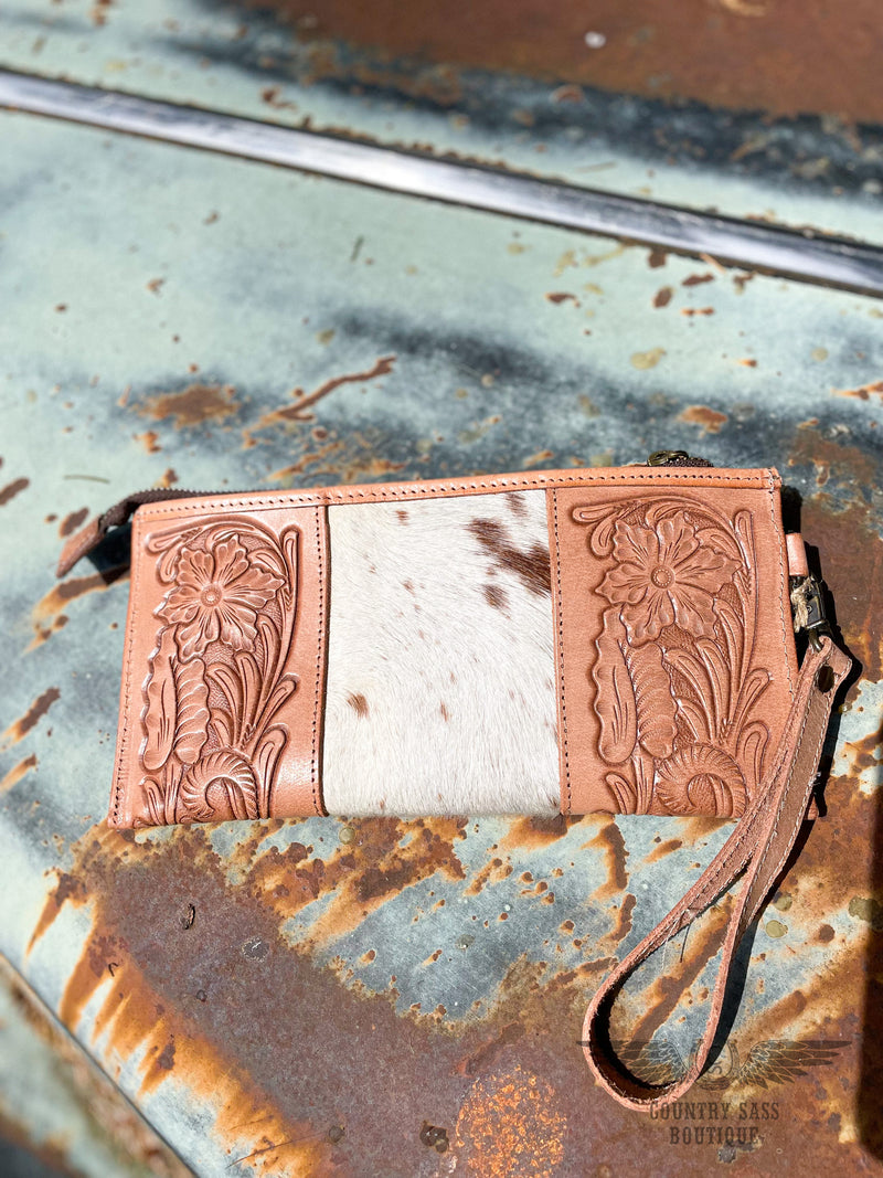 Image of backside of B option of yipee kiyay clutch wallet with veggie tan leather that is stamped with a floral design on each side with white cowhide with brown speckles in the middle.