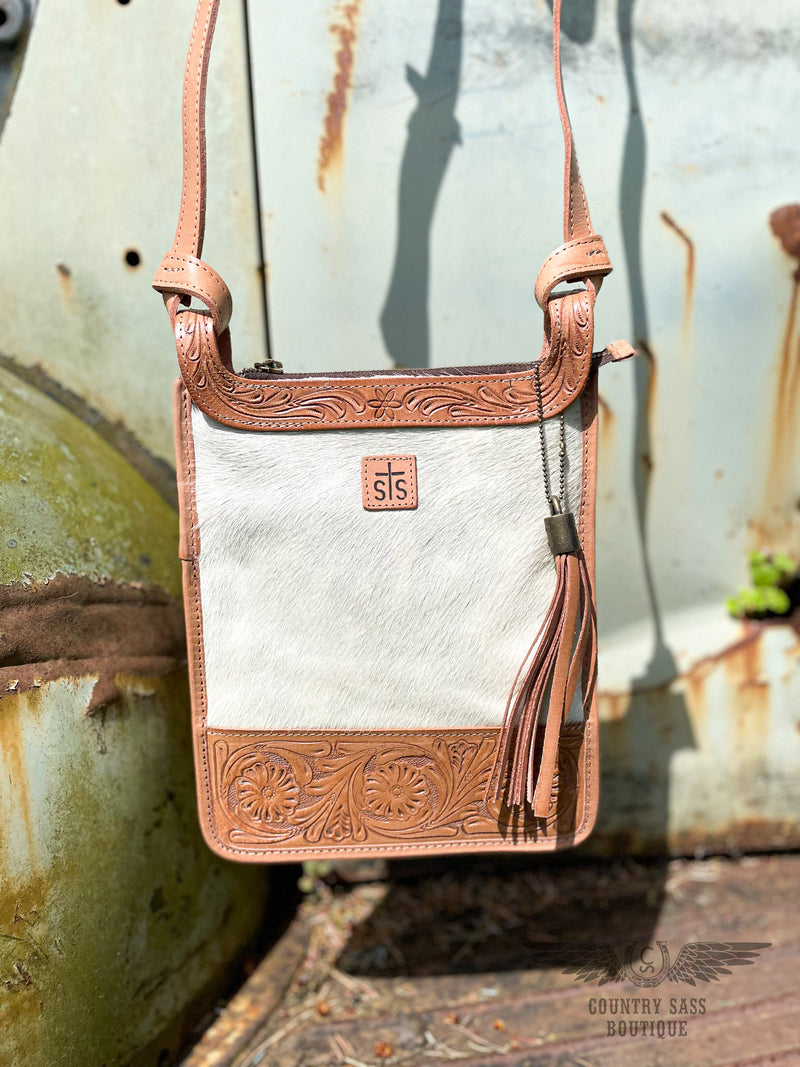 Image of close up of the Yipee Kiyay crossbody purse.  The purse has white cowhide front with floral tooled veggie tan leather detail on the top and bottom.  STS branded leather patch in the middle of the cowhide and removable decorative leather tassel.