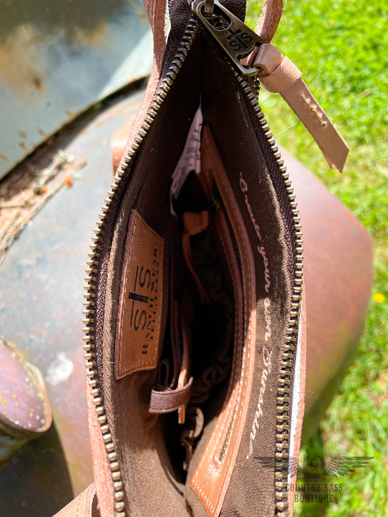 Image of interior of yipee kiyay crossbody purse.  Brown cloth interior with zipper pocket, conceal carry holster, leather branded STS patch and  inspiration quote " Create your own sunshine".  Zipper closure.